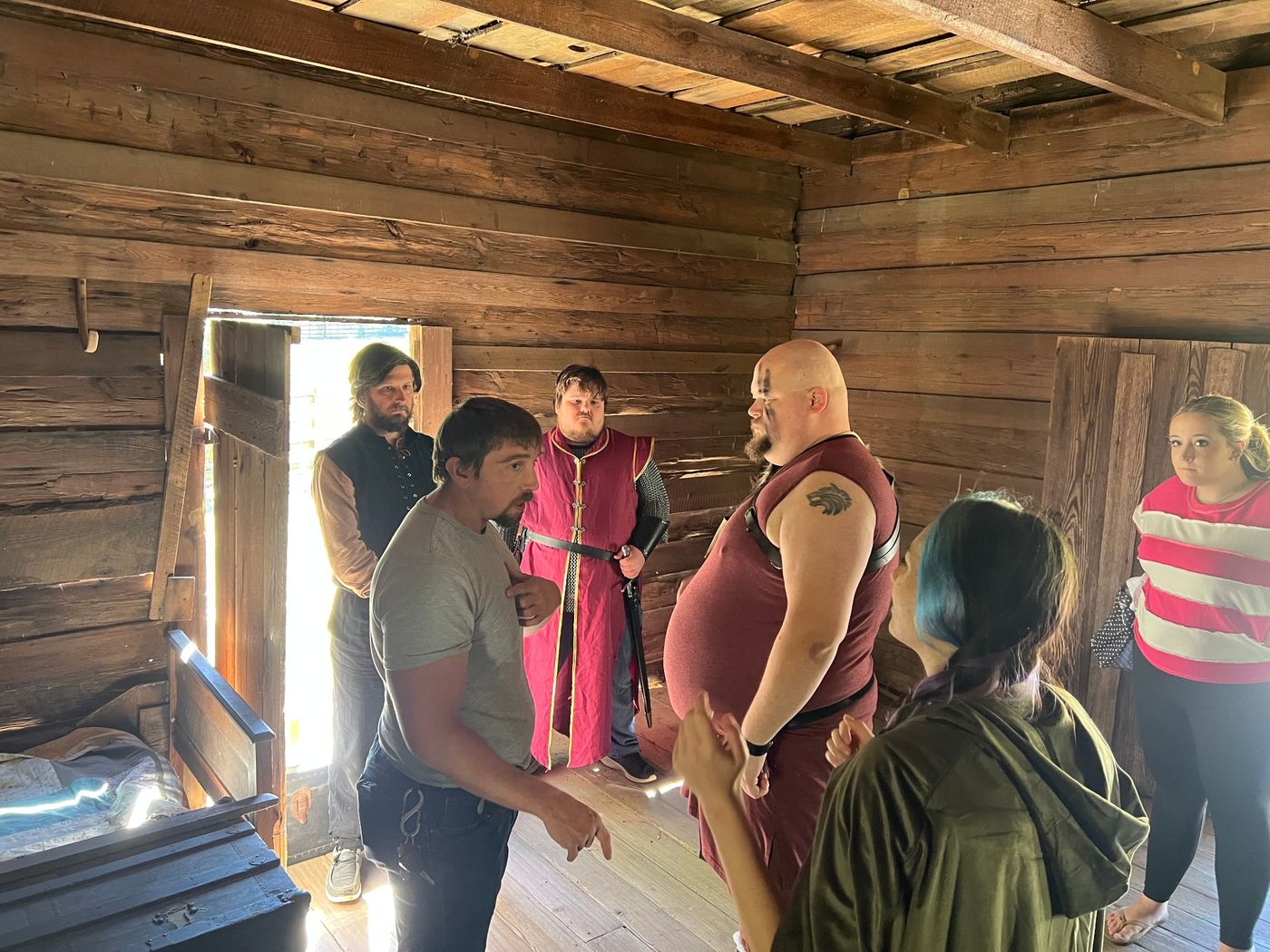 A director working with costumed cast inside a timber cabin