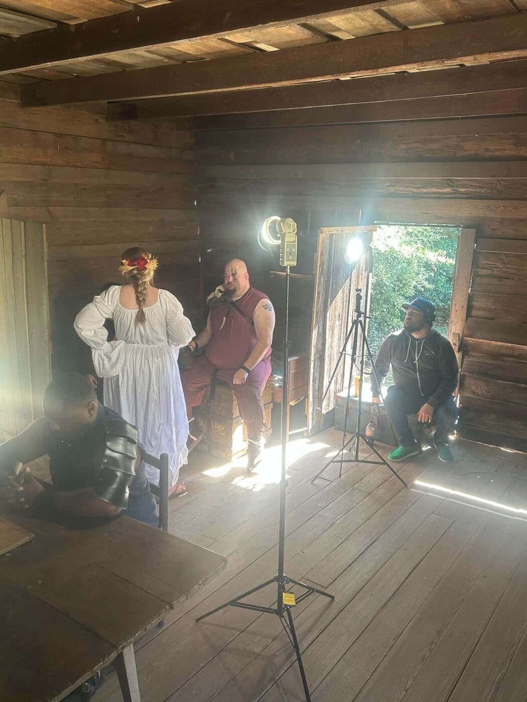 Cast in costume working a scene inside the cabin while crew wait by the light and open door