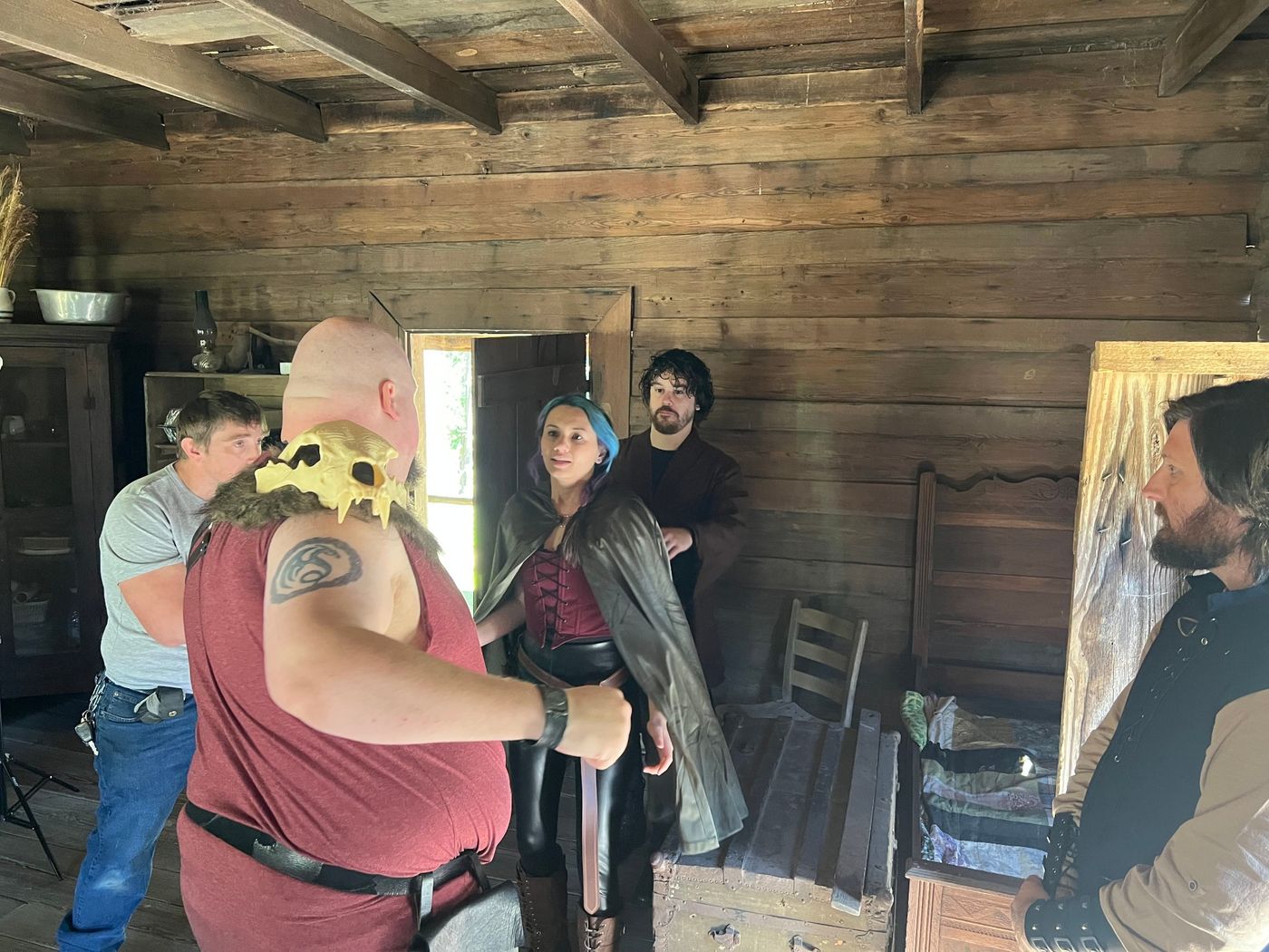 Cast in fantasy costume and crew rehearsing inside a rustic log cabin